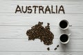 Map of the Australia made of roasted coffee beans laying on white wooden textured background with two coffee cups Royalty Free Stock Photo