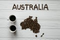 Map of the Australia made of roasted coffee beans laying on white wooden textured background with two coffee cups Royalty Free Stock Photo