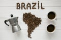 Map of the Brazil made of roasted coffee beans laying on white wooden textured background with two coffe cups and coffee maker Royalty Free Stock Photo