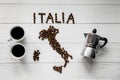 Map of the Italy made of roasted coffee beans laying on white wooden textured background with two cups and coffee maker Royalty Free Stock Photo