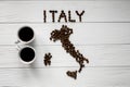 Map of the Italy made of roasted coffee beans laying on white wooden textured background with two cups of coffee Royalty Free Stock Photo