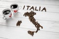 Map of the Italy made of roasted coffee beans laying on white wooden textured background with two cups of coffee Royalty Free Stock Photo