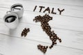 Map of the Italy made of roasted coffee beans laying on white wooden textured background with two cups of coffee Royalty Free Stock Photo