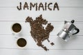 Map of the Jamaica made of roasted coffee beans laying on white wooden textured background with coffee maker and cups of coffee