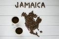 Map of the Jamaica made of roasted coffee beans laying on white wooden textured background with two cups of coffee