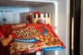 Hand pulls out a Totinos Party Pizza frozen pizza out of freezer. Selective focus on the