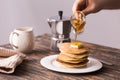 Maple syrup pouring over a stack of mini pancakes.