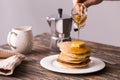 Maple syrup pouring over a stack of mini pancakes.