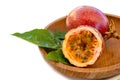 Maracuja cut in half and whole in small glass container peel of the fruit with wooden spoon and leaf on plate and white background