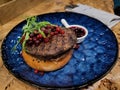 Maral or siberian stag beefsteak minced meat on bun of bread with berry sauce on blur ceramic plate on wooden table