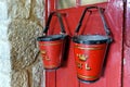 Marazion, Cornwall, UK - April 13 2018: Two old fashioned vintage antique fire buckets hanging on a red door Royalty Free Stock Photo