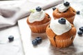 Marble board with tasty muffins, cream and blueberries