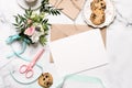 Marble desk with bouquet of flowers, pink scissors, postcard, kraft envelope, cotton branch, oat cookies, invitation card with cop Royalty Free Stock Photo