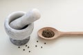 Marble or granite mortar with pestle for manual grinding spices and large wooden spoon with ground pepper on a white kitchen table Royalty Free Stock Photo