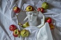 marble head of diana and eye of david reflected in mirror in frame on white drapery fabric with folds with red green apples