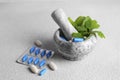 Marble mortar with fresh green herbs and pills on white table, closeup Royalty Free Stock Photo