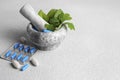 Marble mortar with fresh green herbs and pills on white table, space for text Royalty Free Stock Photo