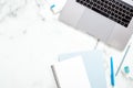 Marble office desk table with laptop computer, paper notepad, blue stationery. Minimal flat lay style composition, top view,