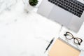 Marble office desk table with laptop computer, paper notepad, glasses, succulent plant, stationery. Minimal flat lay style