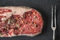 Marble ribeye steak, pepper, sage, fork on blue-black slate