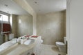 Marble-topped bathroom with a single sink under a large mirror integrated into the wall, white wood cabinets and marble tiles