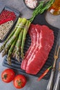 marbled beef bacon. black wooden cutting board with raw marbled beef bacon with asparagus, seasoning tomatoes and