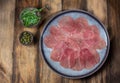 Marbled beef for carpaccio with ingredients arugula and capers on gray plate, wooden background, top view