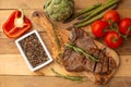 Marbled beef steak on a board with rosemary pepper, seasoning, and fresh vegetables, tomatoes and asparagus, artichoke, on a Royalty Free Stock Photo