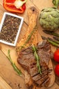 Marbled beef steak on a board with rosemary pepper, seasoning, and fresh vegetables, tomatoes and asparagus, artichoke, on a Royalty Free Stock Photo