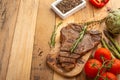 Marbled beef steak on a board with rosemary pepper, spices, and fresh vegetables, tomatoes and asparagus, artichoke, on a wooden Royalty Free Stock Photo