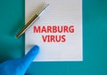 Marburg virus symbol. White note with words Marburg virus, beautiful blue background, doctor hand in blu glove and metallic pen.