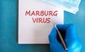 Marburg virus symbol. White note with words Marburg virus, beautiful blue background, doctor hand in blu glove and metallic pen.