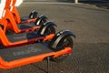 Four orange and black Neuron rent to ride electric scooters with white protective helmets on a pavement sidewalk beside Auckland H