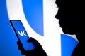 March 23, 2022, Brazil. In this photo illustration, a woman`s silhouette holds a smartphone with the VKontakte VK logo displaye