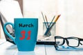 March 31st. Day 31 of month, calendar on morning coffee cup, business office background, workplace with laptop and