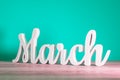 March - wooden carved letters. Beginning of march month, calendar on light turquoise background. Spring coming