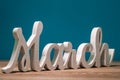 March -word carved of wood. march first spring month, calendar on blue background