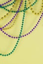 Mardi Gras beads in green, gold and purple hanging, draped in front of a yellow background.