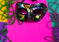 Mardi gras mask and beads in pile on purple background. Royalty Free Stock Photo