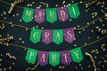 Mardi Gras party golden lettering on paper handmade green and purple festive garland, black background, confetti. Holiday