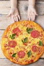 Kids hands hold cheese pizza with tomatoes and basil, vegan meal on wooden rustic table,top view