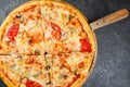 Margarita pizza with chicken mushrooms and tomatoes on a wooden stand on a dark gray background