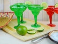 Margaritas in red and green glasses with salted rims and lime garnishes