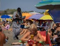 African merchant with beads and other jewelry wears a medical mask on the beach among crowds of people without masks in Marina di