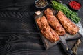 Marinated brisket steaks in bbq sauce on a wooden cutting board with herbs. Black wooden background. Top view. Copy space Royalty Free Stock Photo