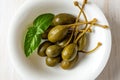 Marinated caper fruits and green basil leaf in a bowl. Pickled caper berries on a white plate. Canned caperberry as garnish and