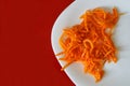Marinated carrots with spices in a white plate on a red background