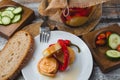 Marinated cheese in olive oil with capsicum in glass jar, fork, plate tomato bread and cucumber on wooden background. Toned photo