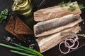 Marinated fillet mackerel or fillet herring fish with spices, greens and slice of bread on plate over dark stone background