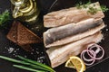 Marinated fillet mackerel or fillet herring fish with spices, greens and slice of bread on plate over dark stone background.